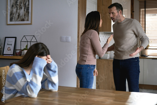 Teenage girl sitting with face in hands and parents arguing in background