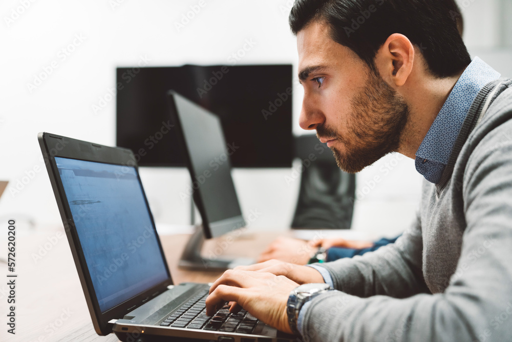 Side view of a focused business man leaning in closer to the laptop screen, coding Side view of a focused business man leaning in closer to the laptop screen, coding