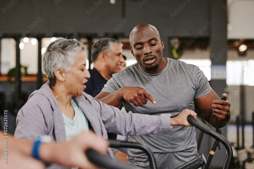 Elderly group, exercise bike and personal trainer for fitness, timer and retirement wellness by blurred background. Senior woman, bicycle training and diversity with black man, progress and coaching