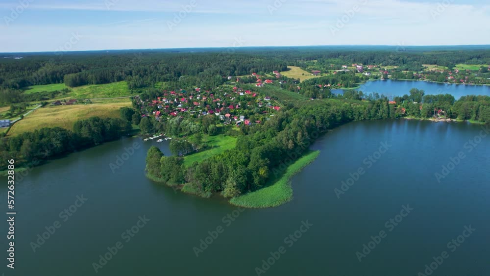 Majestic Aerial View of Calm Lake With Islands in Poland. Impressive Lake Houses. Village Houses on Shore of Paradise Lake. Peaceful Reflected on Water. Cottages Between Green Trees, Forest and Hills. Majestic Aerial View of Calm Lake With Islands in Poland. Impressive Lake Houses. Village Houses on Shore of Paradise Lake. Peaceful Reflected on Water. Cottages Between Green Trees, Forest and Hills.