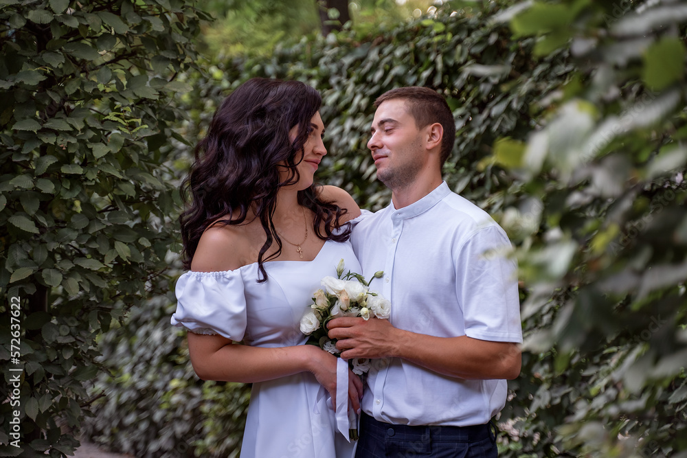 A stylish white young couple smiles at each other. Portrait of secluded young people. Newlyweds hid in the bushes. Selective focus A stylish white young couple smiles at each other. Portrait of secluded young people. Newlyweds hid in the bushes. Selective focus