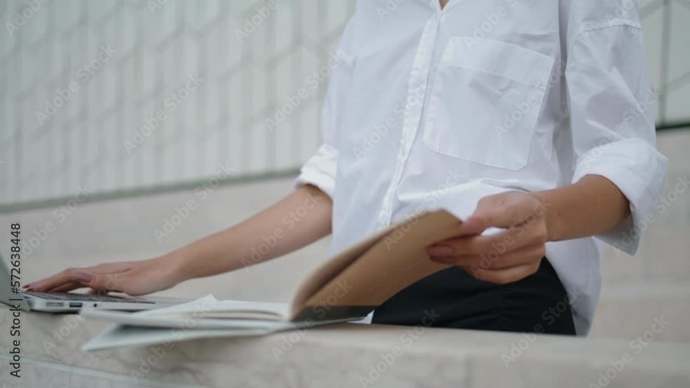 Woman hands typing laptop taking data from work notes outdoors close up. Woman hands typing laptop taking data from work notes outdoors close up.