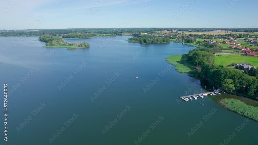 Majestic Aerial View of Calm Lake With Islands in Poland. Impressive Lake Houses. Village Houses on Shore of Paradise Lake. Peaceful Reflected on Water. Cottages Between Green Trees, Forest and Hills. Majestic Aerial View of Calm Lake With Islands in Poland. Impressive Lake Houses. Village Houses on Shore of Paradise Lake. Peaceful Reflected on Water. Cottages Between Green Trees, Forest and Hills.