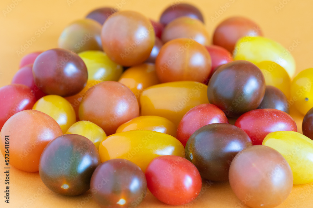 Cherry tomatoes in a variety of bright colors on an orange background. Cherry tomatoes in a variety of bright colors on an orange background.