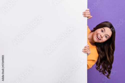 Photo of pretty excited lady wear orange sweatshirt holding white wall empty space isolated violet color background