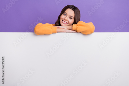 Photo of pretty sweet girl dressed orange sweatshirt holding white billboard empty space isolated purple color background