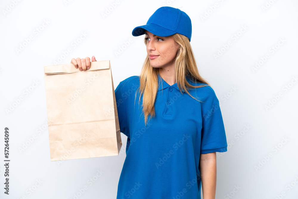 Young Uruguayan woman taking a bag of takeaway food isolated on white background looking to the side Young Uruguayan woman taking a bag of takeaway food isolated on white background looking to the side