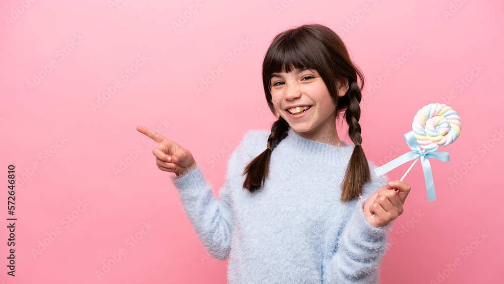 Little caucasian girl holding a lollipop pointing finger to the side Little caucasian girl holding a lollipop pointing finger to the side