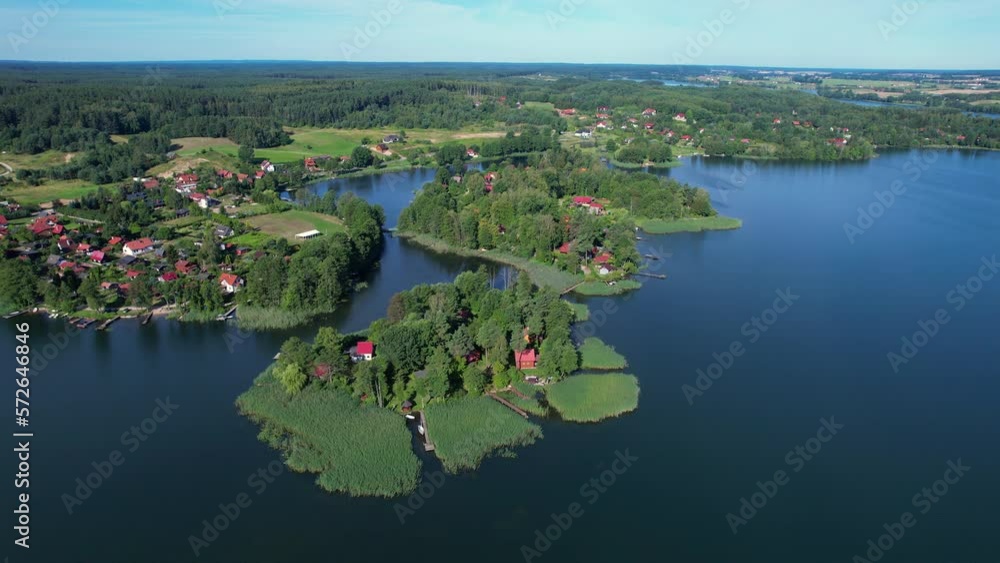 Majestic Aerial View of Calm Lake With Islands in Poland. Impressive Lake Houses. Village Houses on Shore of Paradise Lake. Peaceful Reflected on Water. Cottages Between Green Trees, Forest and Hills. Majestic Aerial View of Calm Lake With Islands in Poland. Impressive Lake Houses. Village Houses on Shore of Paradise Lake. Peaceful Reflected on Water. Cottages Between Green Trees, Forest and Hills.