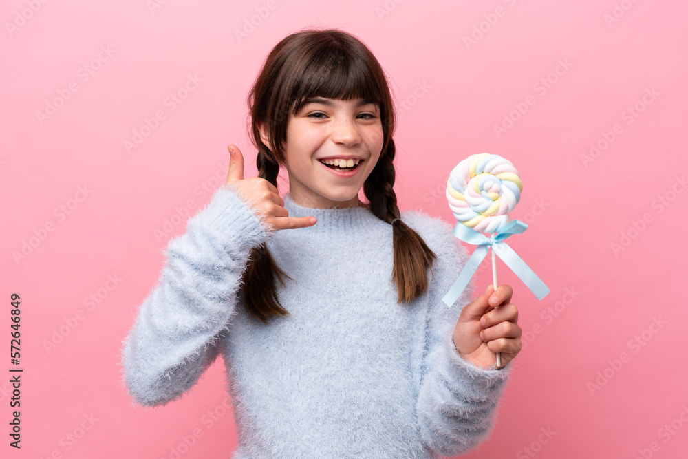 Little caucasian girl holding a lollipop making phone gesture. Call me back sign Little caucasian girl holding a lollipop making phone gesture. Call me back sign
