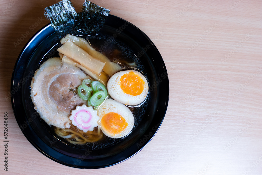 Soy sauce ramen in a black cup topped with chashu pork, Naruto fish