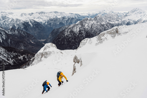 Snowy white Alps and a couple of ski tourers climbing up the mountain to ski back down