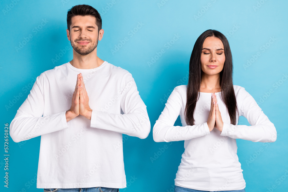 Portrait of two peaceful relaxed positive people couple dressed white shirts meditating eyes close isolated on blue color background Portrait of two peaceful relaxed positive people couple dressed white shirts meditating eyes close isolated on blue color background