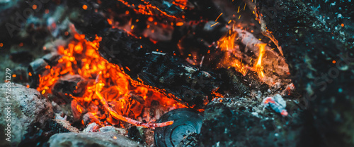 Vivid smoldered firewoods burned in fire closeup. Atmospheric background with orange flame of campfire. Full frame image of bonfire with sparks in bokeh. Warm vortex of glowing embers and ashes in air