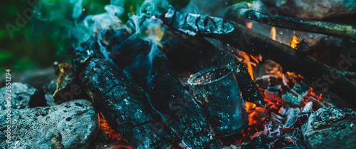 Vivid smoldered firewoods burned in fire close-up. Atmospheric warm background with orange flame of campfire and blue smoke. Unimaginable full frame image of bonfire. Burning logs in beautiful fire.