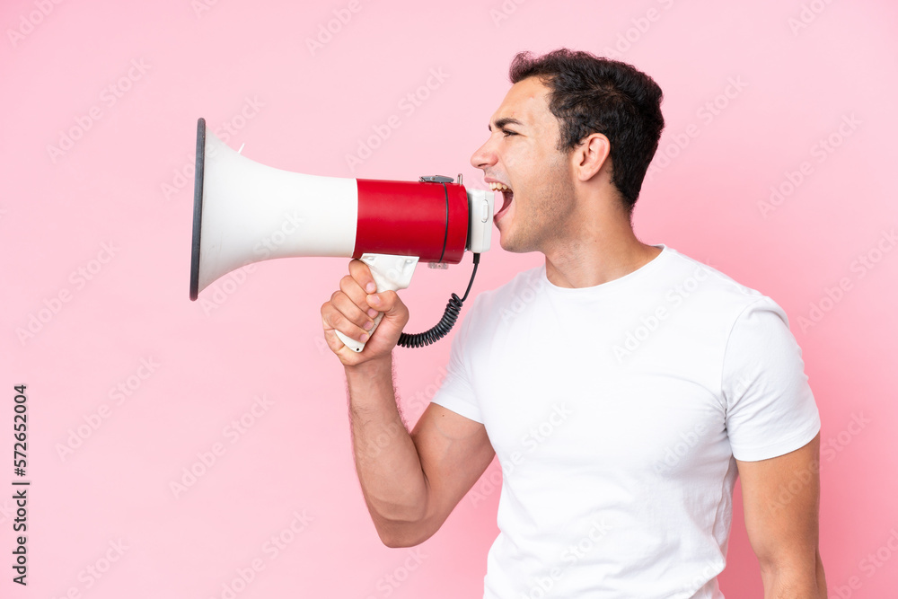 Young caucasian man isolated on pink background shouting through a megaphone to announce something in lateral position Young caucasian man isolated on pink background shouting through a megaphone to announce something in lateral position