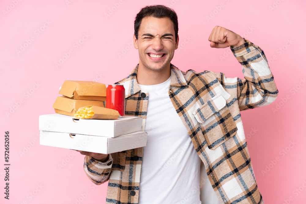 Young caucasian man holding fast food isolated on pink background doing strong gesture Young caucasian man holding fast food isolated on pink background doing strong gesture