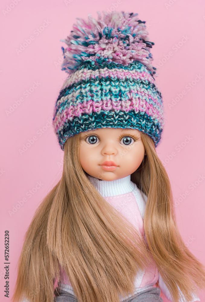 Beautiful vinyl doll with a cute baby face in a bright knitted hat close-up portrait, modern toys, knitted clothes, selective focus Beautiful vinyl doll with a cute baby face in a bright knitted hat close-up portrait, modern toys, knitted clothes, selective focus
