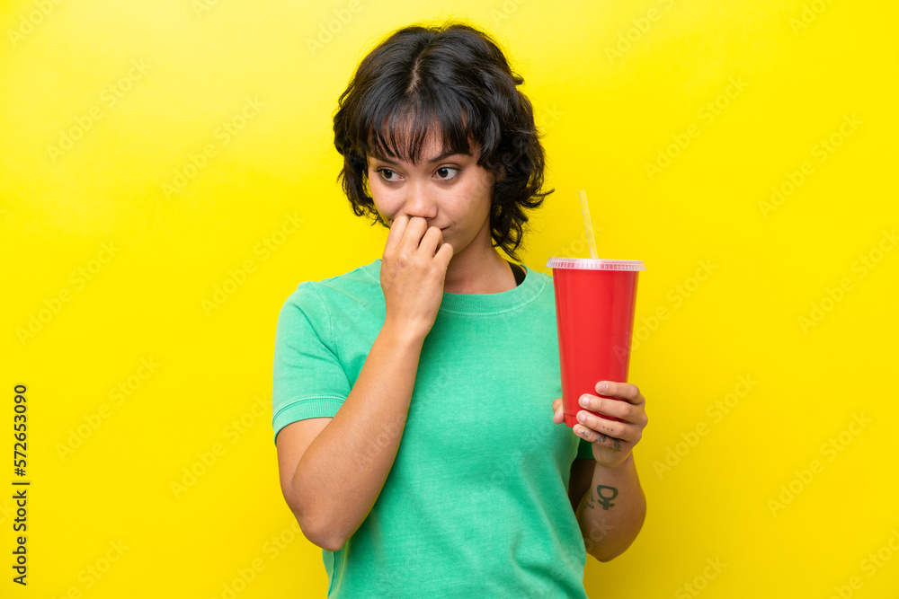 Young Argentinian woman holding a soda isolated on yellow background having doubts Young Argentinian woman holding a soda isolated on yellow background having doubts