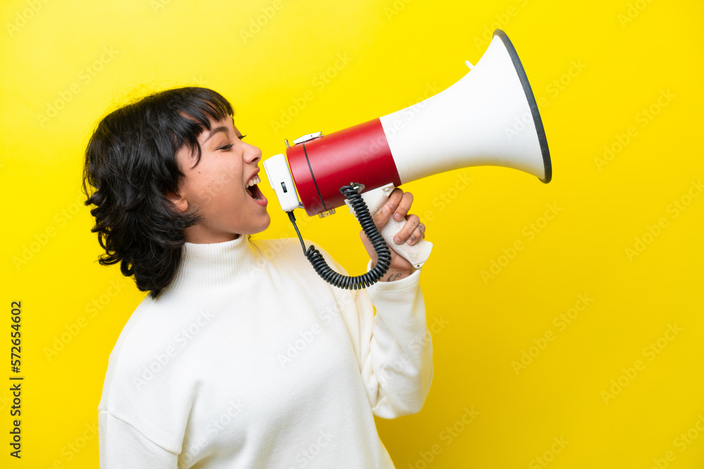 Young Argentinian woman isolated on yellow background shouting through a megaphone to announce something in lateral position Young Argentinian woman isolated on yellow background shouting through a megaphone to announce something in lateral position