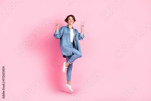 Full length photo of pretty cute lady dressed denim jacket jumping high showing v-signs isolated pink color background