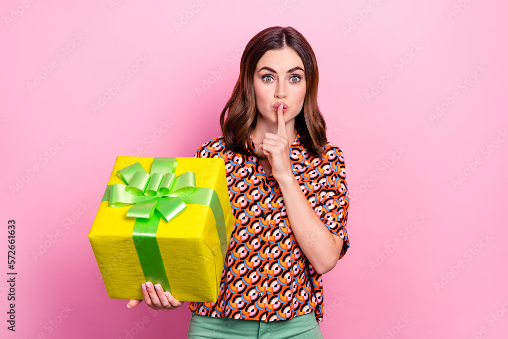 Photo of youngster woman brown hair pouted lips secret sign finger wear stylish shirt hold package keep secret isolated on pink color background