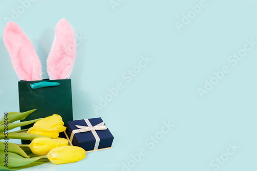 Easter card with a gift box, a bouquet of tulips and rabbit ears in a green paper bag on a blue background. place for text. High quality photo