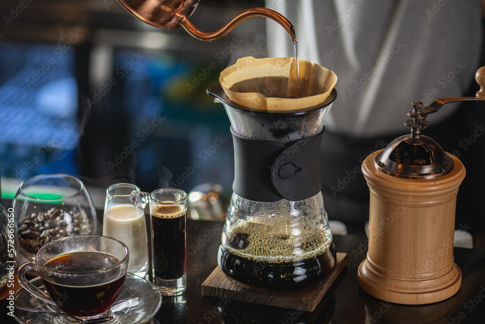 drip coffee, Barista making drip coffee by pouring spills hot water on coffee ground with prepare filter from copper pot to glass transparent chrome drip maker on wooden table in cafe shop drip coffee, Barista making drip coffee by pouring spills hot water on coffee ground with prepare filter from copper pot to glass transparent chrome drip maker on wooden table in cafe shop