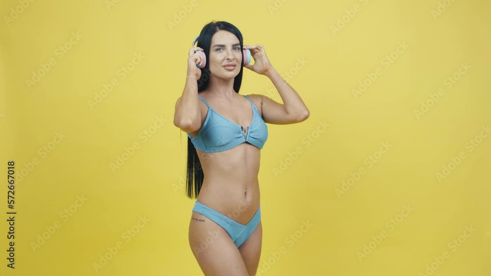 Beautiful young woman in headphones on a yellow background listening to music and dancing. Posing in the studio Beautiful young woman in headphones on a yellow background listening to music and dancing. Posing in the studio