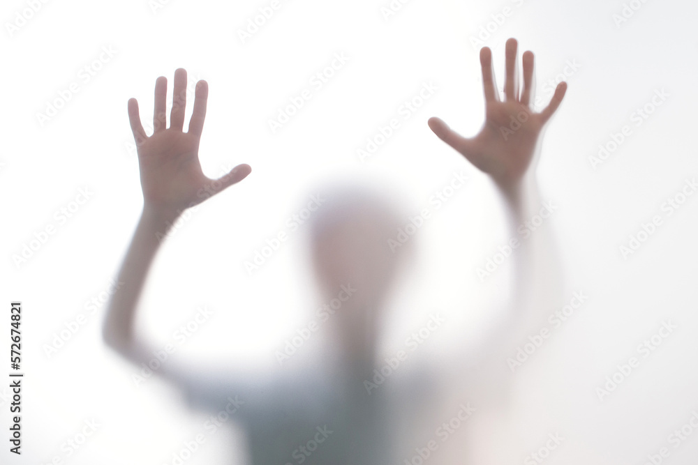 Silhouette scared boy stand behind glass door. Kid showing two hands.