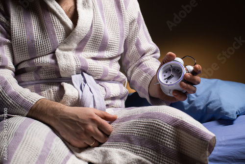 Andropause concept. An unrecognizable man in a bathrobe holds an alarm clock in his hand. Male menopause, impotence, biological clock. photo