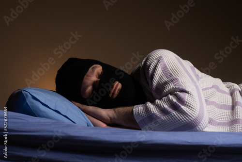 The robber in the mask lies in bed and sleeps. The thief is tired. Night adventure dreams playful concept.
