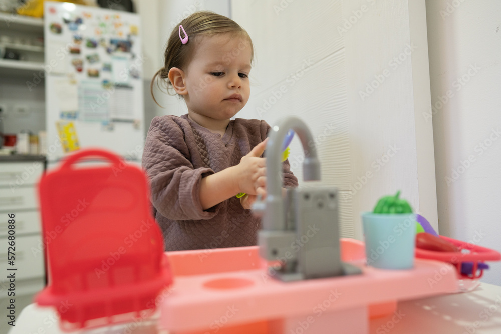 One little toddler girl playing in the kitchen with her toy dishwasher, early child development concept One little toddler girl playing in the kitchen with her toy dishwasher, early child development concept