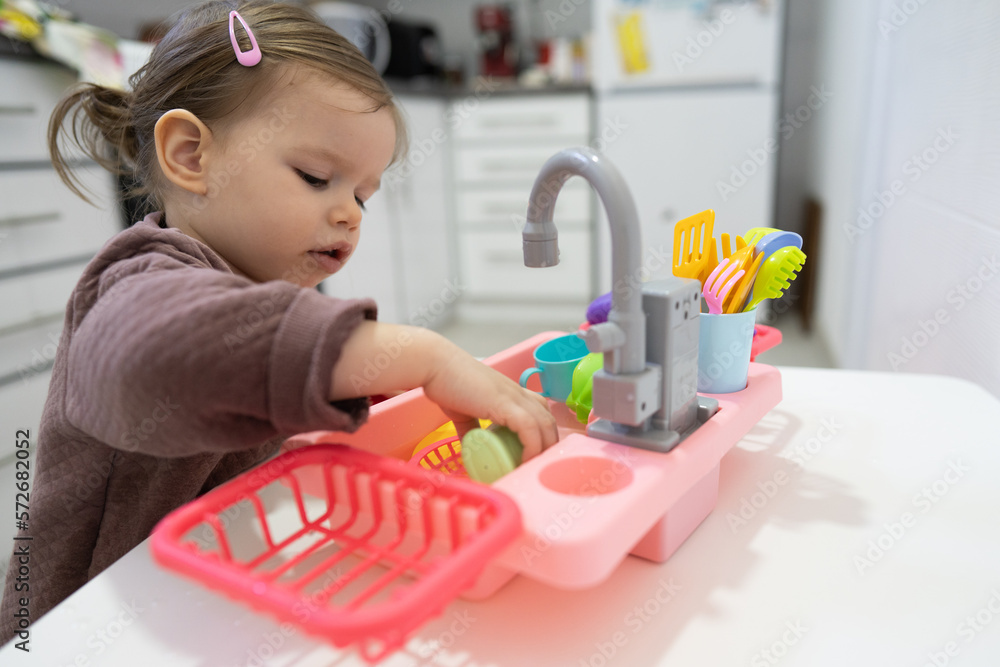 One little toddler girl playing in the kitchen with her toy dishwasher, early child development concept One little toddler girl playing in the kitchen with her toy dishwasher, early child development concept