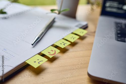 Lachende und traurige Gesichter auf post it Zettel in einem Notizbuch auf einem Schreibtisch aus Holz. 