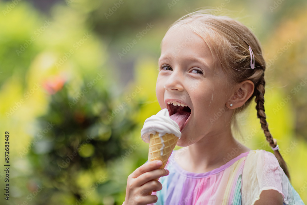 Pretty little caucasian girl with blonde hair eight years old eating licking vanilla ice cream in waffles cone outdoor at hot summer day
