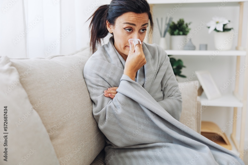 Woman cold headache runny nose and stuffy nose sitting on sofa in plaid, treatment for flu, allergies and covid-19 Woman cold headache runny nose and stuffy nose sitting on sofa in plaid, treatment for flu, allergies and covid-19