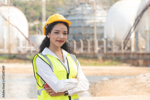 female engineer with hardhat with petrochemical factory background. asian woman holding tablet, plan and Walkie Talkie.