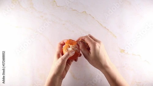 Womans hands peeling a clementine orange, top view on marble table