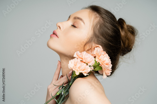 Young woman with carnations touching neck isolated on grey. photo