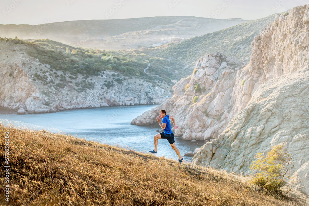 middle-aged man running uphill on trail in background of sea bay and mountains