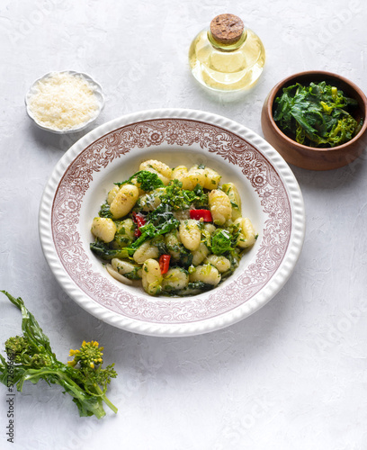 Gnocchi with  turnip leaves and tops or cima di rapa with chili pepper, olive oil and  Parmesan cheese.  Mix  recipes of south, Puglia, and nord of Italy.  White table, front view,  vintage dish
 photo