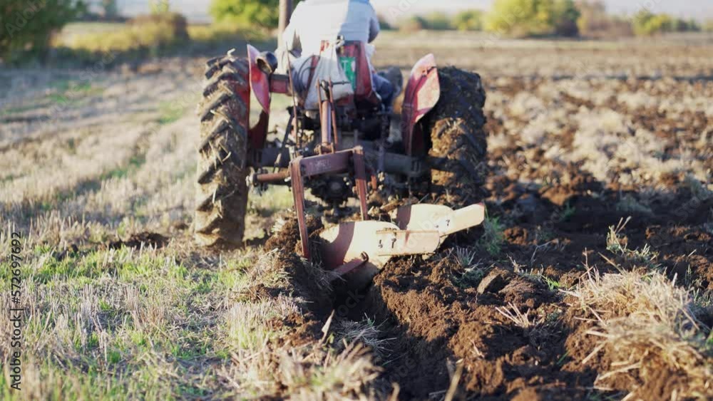 Farmer in tractor preparing farmland with seedbed for the next year, slow motion, selective focus to plowing blades Farmer in tractor preparing farmland with seedbed for the next year, slow motion, selective focus to plowing blades