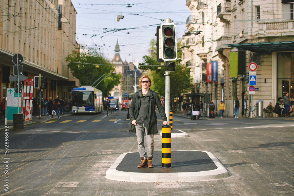 Outdoor portrait of handsome young man posing in the middle of the road next to traffic light