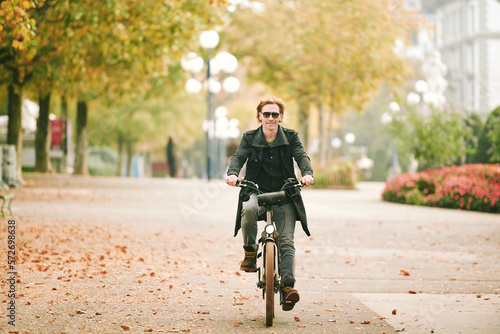 Outdoor portrait of handsome read-haired man riding bike in a city