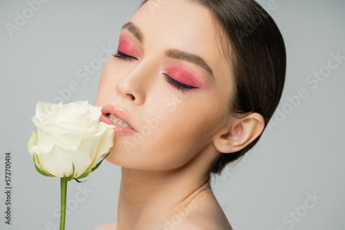 portrait of pretty woman with pink eye shadows near fresh rose isolated on grey.
