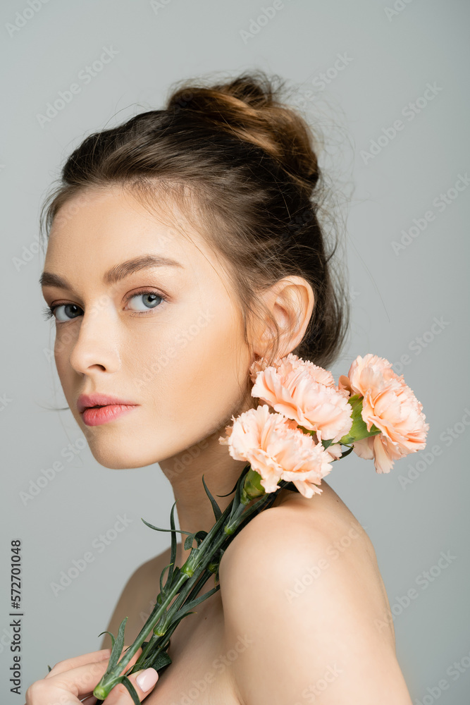 Young fair haired woman with naked shoulders holding carnations isolated on grey.