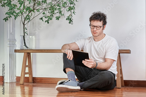 Portrait of a young white man sitting on floor and working with a tablet photo