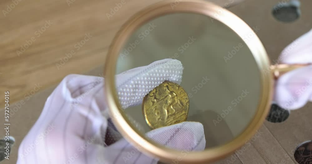 Hands in gloves hold an ancient coin and a magnifying glass