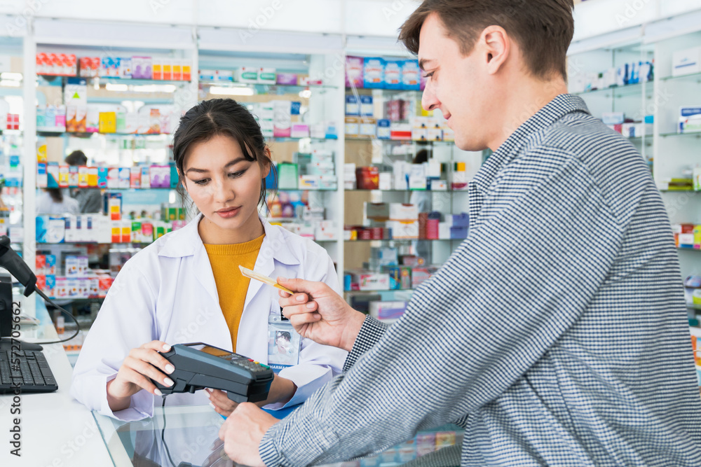 Payment by credit card with payment terminal in qualified drugstore. Modern financial payment of electric money. Caucasian customer purchase medication in pharmacy with prescription from pharmacist. - obrazy, fototapety, plakaty 